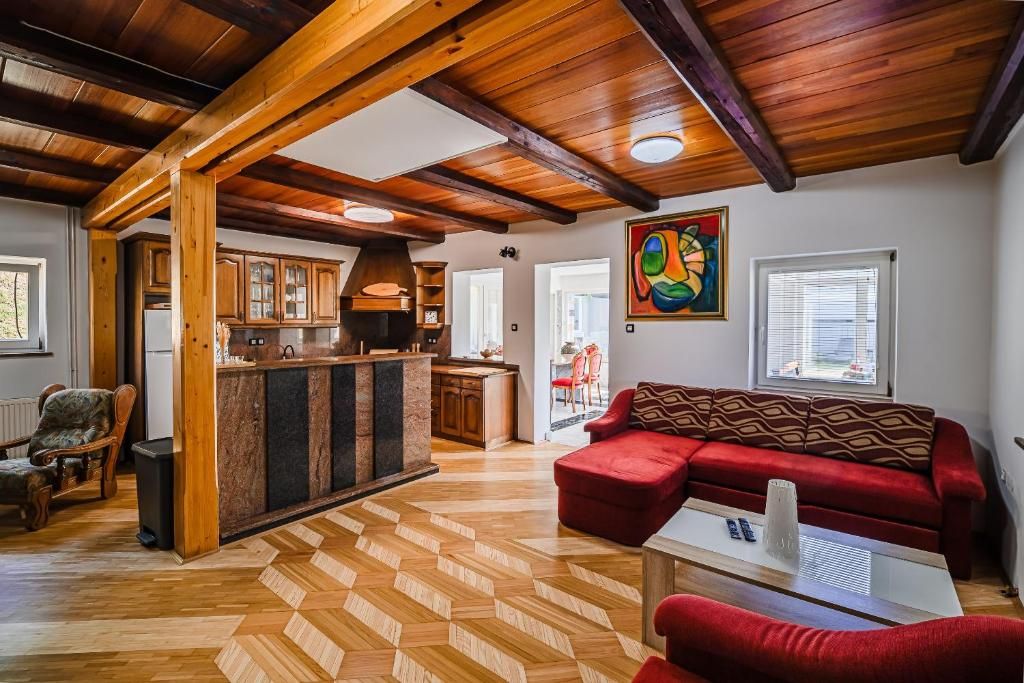 A spacious living area with a herringbone floor pattern, a red sofa, and a wooden ceiling.