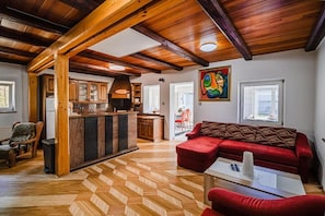 Uma sala de estar ampla com padrão de piso em herringbone, um sofá vermelho e teto de madeira.