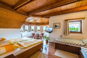 Une pièce avec un plafond en bois, un lit, un canapé, une télévision, une table avec des chaises et une fenêtre avec des rideaux.