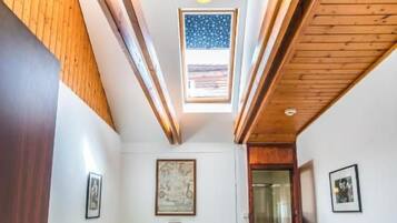 A bedroom with a wooden ceiling, a bed with a headboard, a window, and a door.