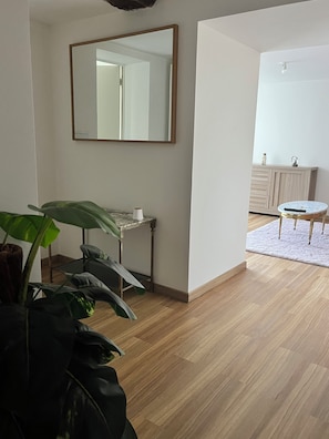 Una habitación con piso de madera, un espejo, una mesita, una silla y una planta en maceta.