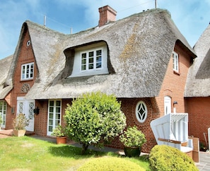 A traditional thatched-roof cottage with a brick facade, a small front garden with potted plants, and a white chair outside. - Fabian Vacation Rental - 3-room vacation rental in Kampen for 5 people with a terrace, (Kampen (Sylt))