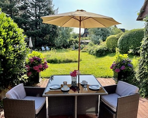An outdoor dining area with a table set for two, surrounded by wicker furniture, under a large umbrella. - Fabian Vacation Rental - 3-room vacation rental in Kampen for 5 people with a terrace, (Kampen (Sylt))