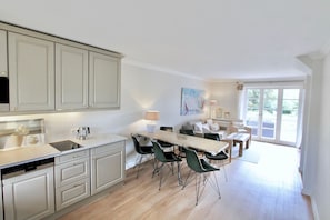 A modern kitchen with a dining area, featuring a large table and chairs, a built-in oven, and a view through the glass door. - Fabian Vacation Rental - 3-room vacation rental in Kampen for 5 people with a terrace, (Kampen (Sylt))