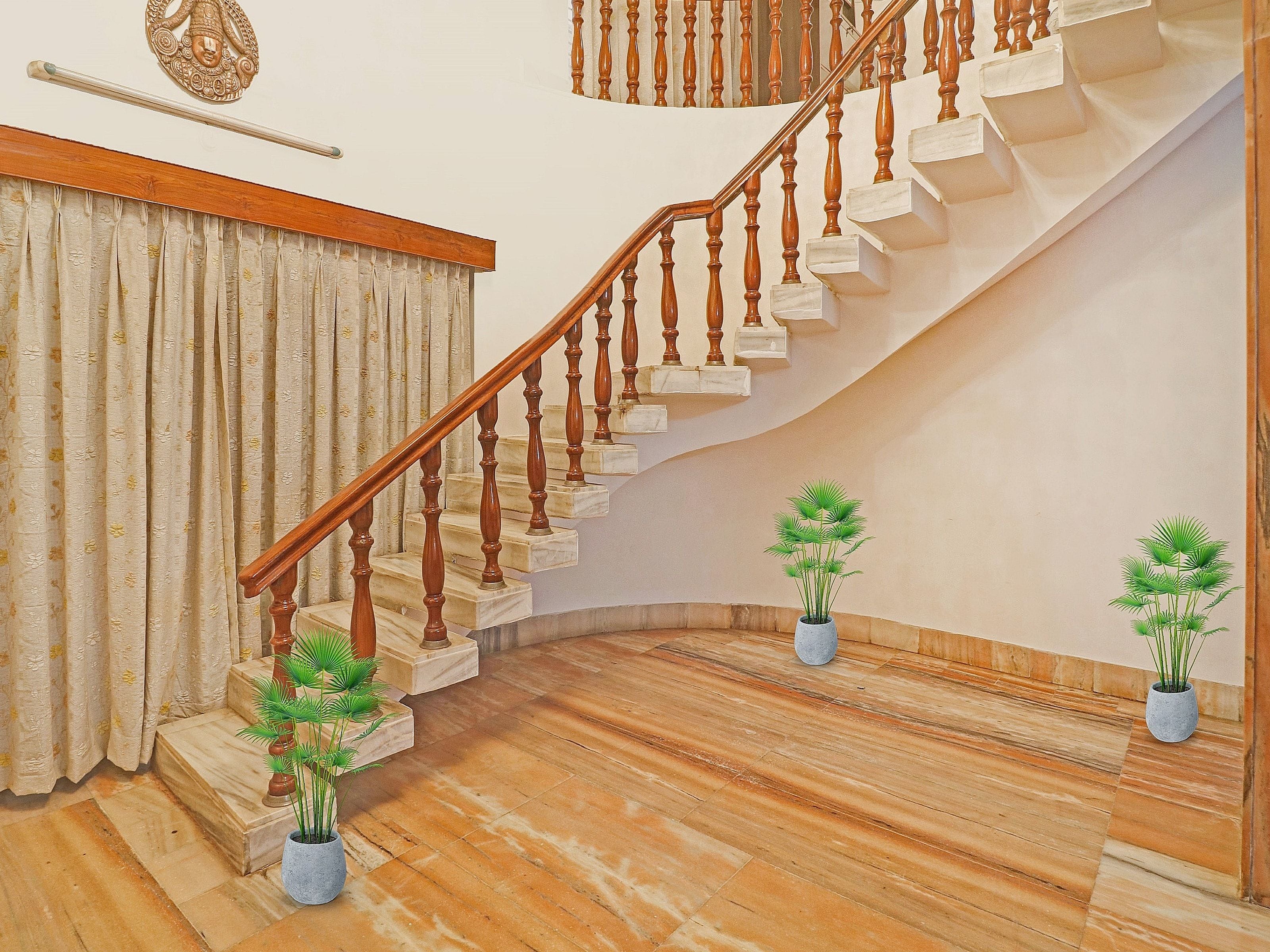 A staircase with wooden balusters and marble steps, flanked by potted plants and a curtain.