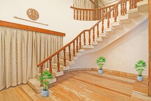 A staircase with wooden balusters and marble steps, a curtain with a floral pattern, and two potted plants.