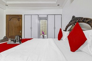 A hotel room with a bed, a wooden door, a wardrobe, and a mirror with an ornate frame. - Super Hotel O Alpine Glow Crest (Hyderabad)