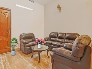 A living room with a brown leather sofa, a small round table with a vase of flowers, and a wooden door.