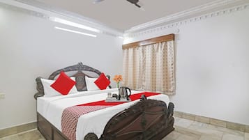 A neatly made bed with a decorative headboard, a bedside table with a tray of items, and a window with curtains.