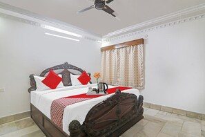A neatly made bed with a decorative headboard, a bedside table with a tray of items, and a window with curtains. - Super Hotel O Alpine Glow Crest (Hyderabad)