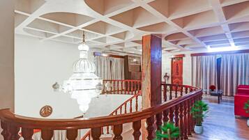 A spacious interior with a grand staircase, a chandelier, and a view of a room with a red sofa and curtains.