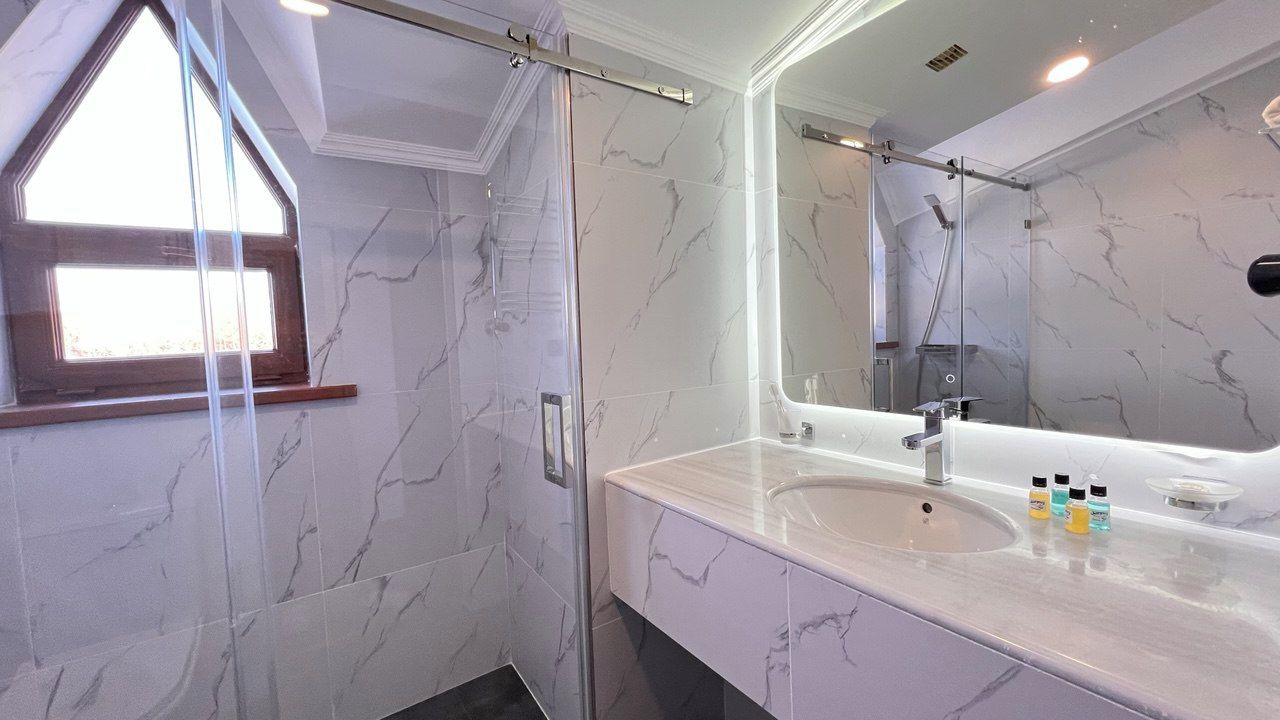 A bathroom with a shower, a sink with a mirror, and marble tiles.