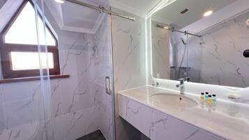 A bathroom with a shower, a sink with a mirror, and marble tiles.