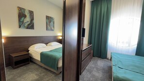 A hotel room with a bed, bedside table, dresser, and a view of the outside through a window. - hotel Kapriz Karakol (Karakol)