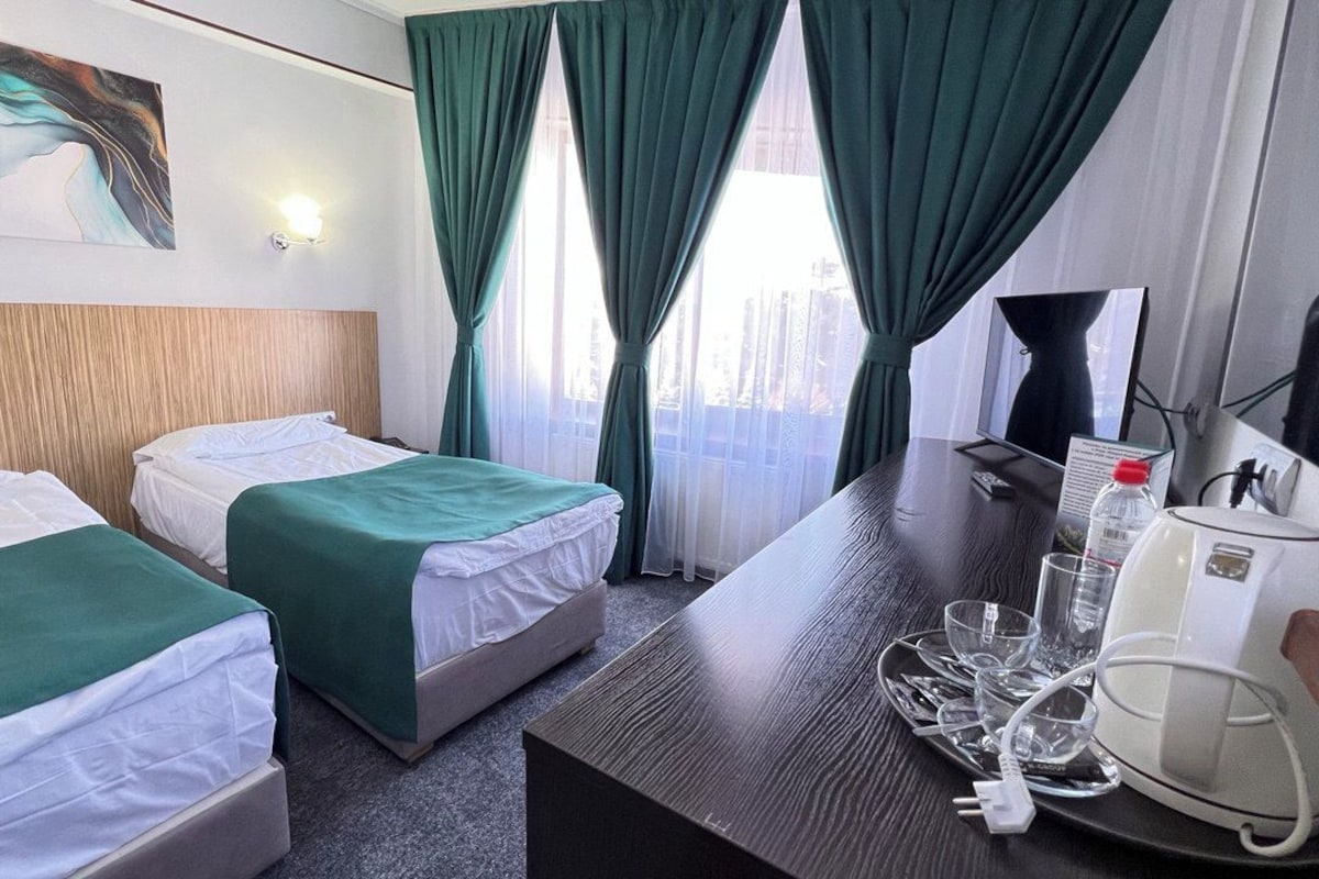 A hotel room with two beds, a desk with a coffee maker, and a view of the city through the window.