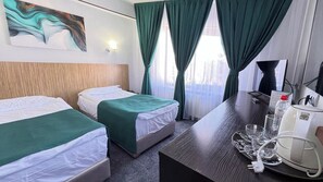 A hotel room with two beds, a desk with a coffee maker, and a view of the city through the window. - hotel Kapriz Karakol (Karakol)
