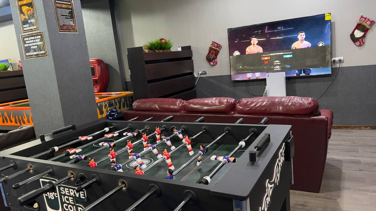 A room with a foosball table, a television mounted on the wall, and a seating area with a red couch.