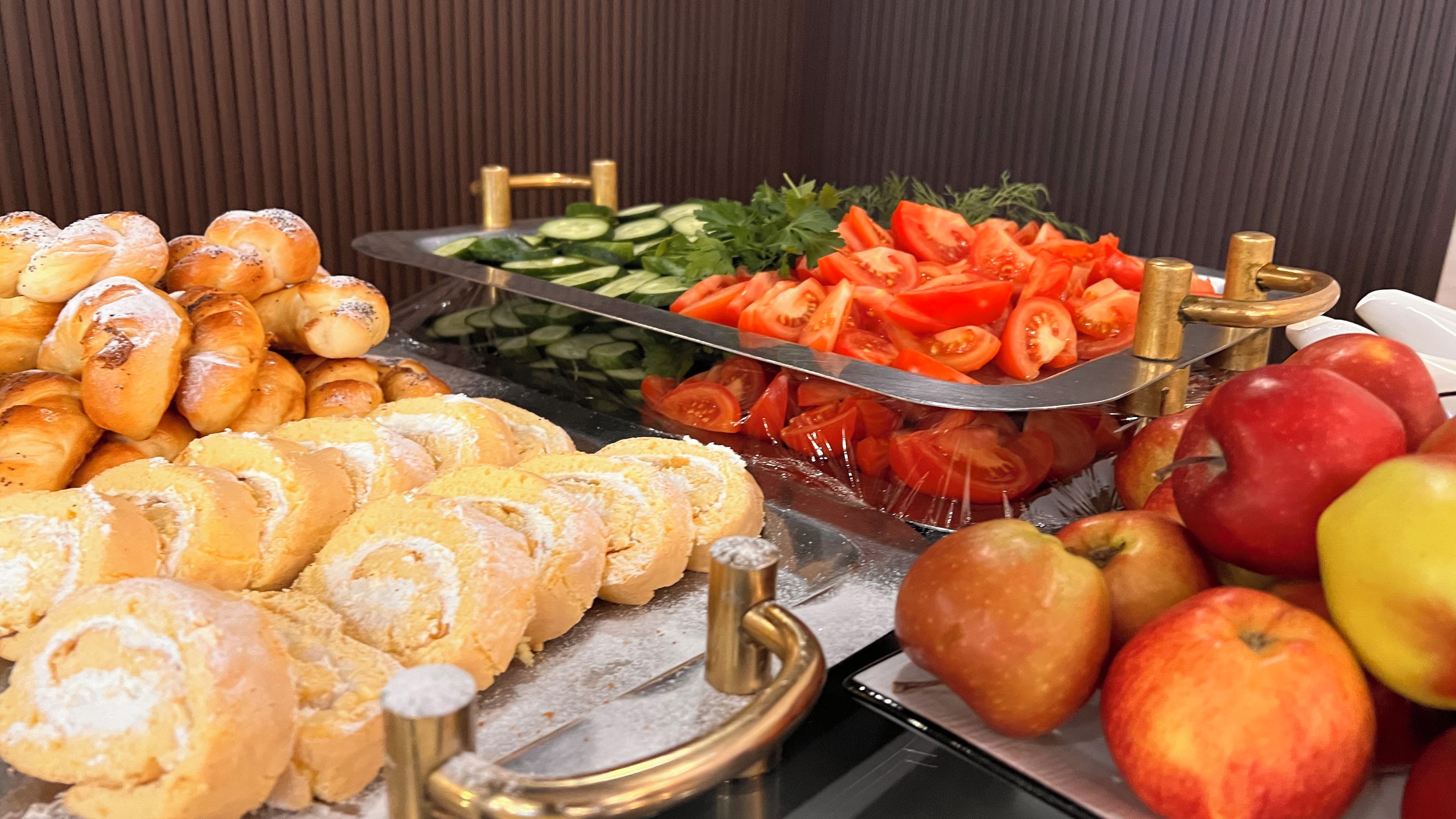 A buffet with various food items including bread, sliced tomatoes, cucumbers, and apples.