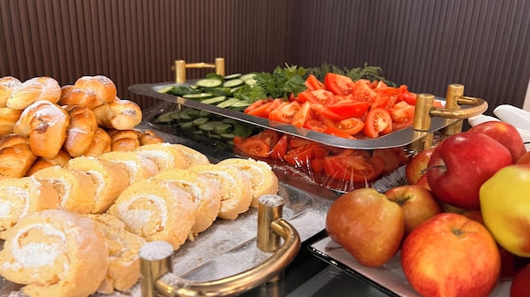 A buffet with various food items including bread, sliced tomatoes, cucumbers, and apples. - hotel Kapriz Karakol (Karakol)