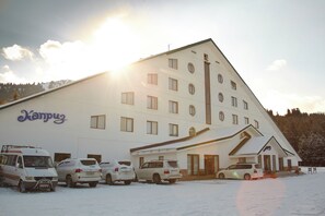 A multi-story building with a flat roof and several windows, a sign reading 'Kampuz,' and parked cars in front. - hotel Kapriz Karakol (Karakol)