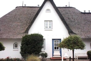 A white building with a steeply pitched thatched roof, a small window, and a door with a blue frame. - Holiday apartment in Sylt with swimming pool (Sylt)