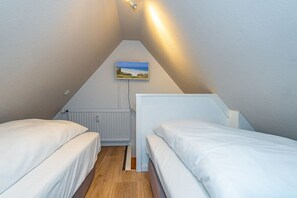 A small, triangular attic bedroom with two beds, a radiator, and a picture on the wall. - Holiday apartment in Sylt with swimming pool (Sylt)