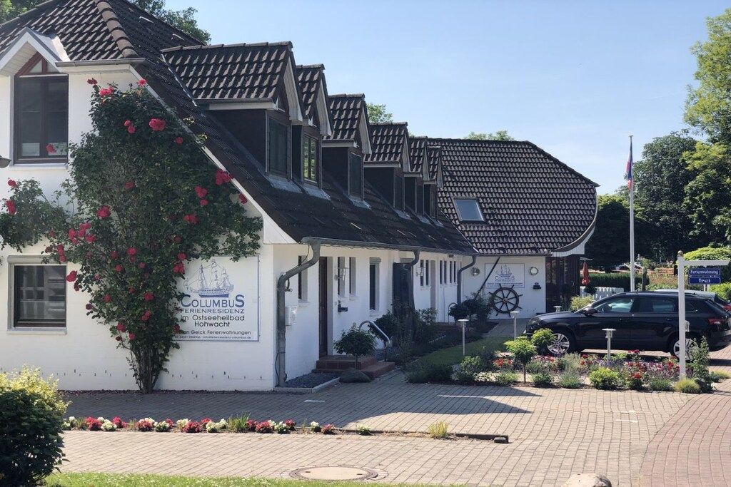 Un edificio blanco con un letrero que indica que es el Hotel Columbus. Hay un jardín con flores en la parte delantera del edificio.