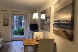 A dining area with a wooden table, two chairs, a chandelier, and artwork on the walls. - Holiday apartment with 1 bedroom (Hohwacht)