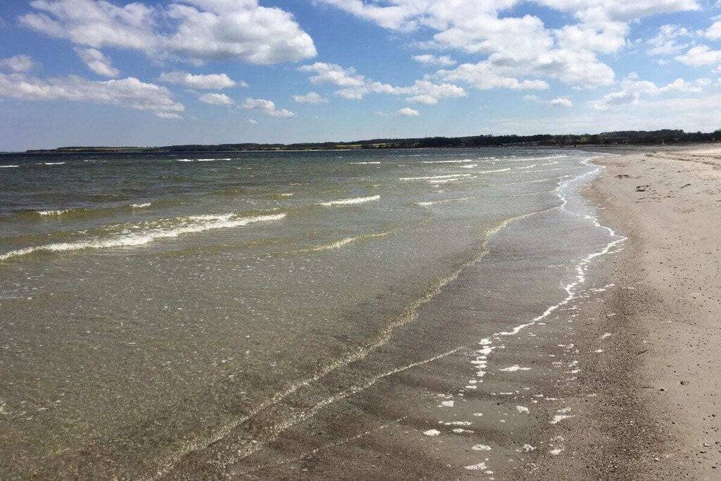 A beach with clear water, a sandy shore, and a distant shoreline.