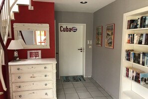 A hallway with a staircase, a door labeled 'Cuba,' a bookshelf with books, and a mirror. - Holiday apartment with 1 bedroom (Hohwacht)
