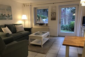 Een woonkamer met een bank, een salontafel, een tv-meubel en een raam met uitzicht op groen.