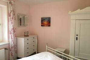 Een slaapkamer met een bed, een dressoir, een nachtkastje, een kledingkast en een schilderij aan de muur.