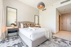A hotel room with a large bed, two bedside tables, a mirror, and a hanging light fixture. - Relaxing 2BR with Balcony Facing the Community, Minutes by Car to the Mall (Dubai)