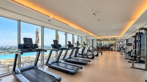A gym with treadmills, exercise bikes, and weight machines, large windows with a city view, and a ceiling with recessed lighting. - Relaxing 2BR with Balcony Facing the Community, Minutes by Car to the Mall (Dubai)