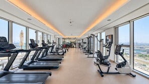 Et fitnesscenter med løbebånd, motionscykler og styrkemaskiner, store vinduer og udsigt over byen.