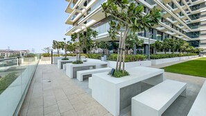 A modern building with a glass facade, outdoor seating areas, and a well-maintained lawn. - Relaxing 2BR with Balcony Facing the Community, Minutes by Car to the Mall (Dubai)