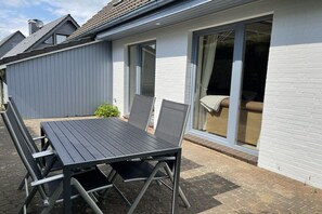 An outdoor patio with a table and chairs, a sliding glass door, and a white brick wall. - Holiday home in Langholz with barbecue (Langholz)