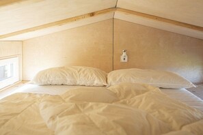 Ein Schlafzimmer mit geneigter Decke, einem Fenster und einem Bett mit weißer Bettwäsche.