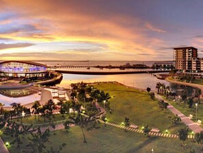 A waterfront hotel with a large glass building, a grassy area with pathways, and a view of the water. - Two Bedroom Apartment In The Heart Of Darwin (Darwin)