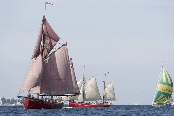Eine Segelyacht mit mehreren Segeln, einem roten Rumpf und einer Flagge auf dem Mast.