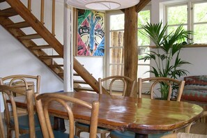 Ein Essbereich mit Holztisch und -stühlen, einer Treppe, einem farbenfrohen Gemälde und einer großen Pflanze.