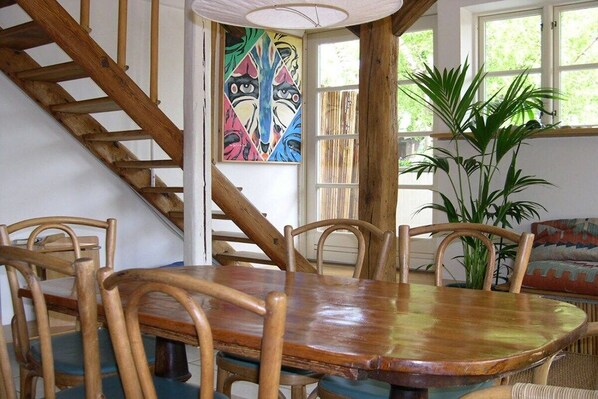 A dining area with a wooden table and chairs, a staircase, a colorful painting, and a large plant. - Holiday apartment with 1 bedroom (Lutterbek)
