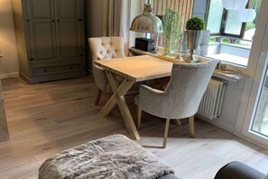 A dining area with a wooden table, two chairs, a lamp, and a window with a view. - holiday apartment Hahnenklee Apartment 2 (Goslar Hahnenklee)