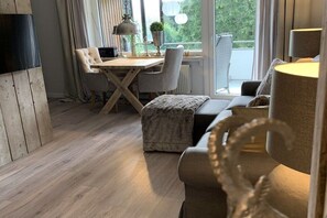 Ein modernes Wohnzimmer mit Holzboden, einer Couch, einem Esstisch mit Stühlen und Blick auf Grünflächen.