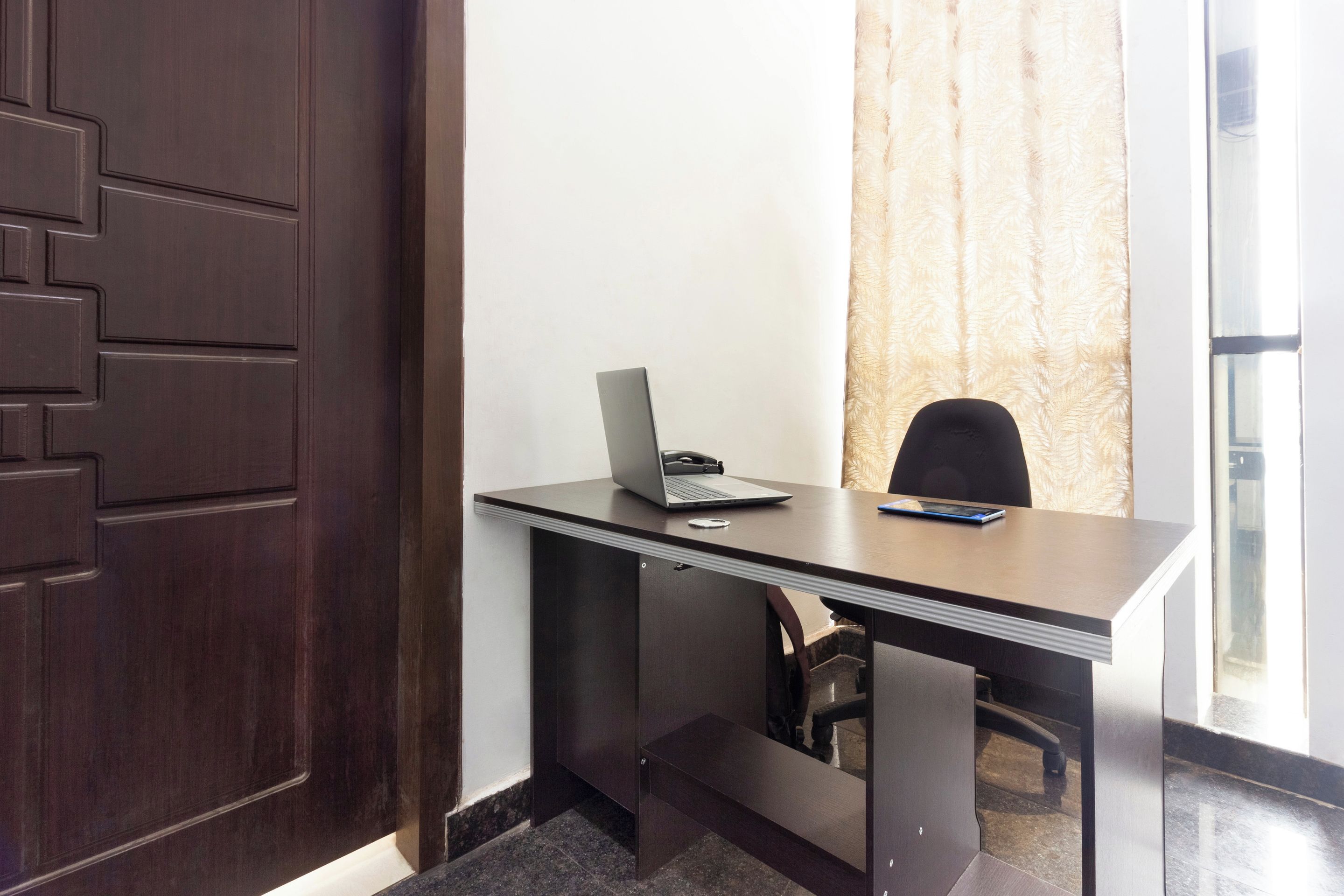 Una habitación con escritorio, silla, laptop y teléfono.
