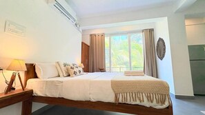 Ein Hotelzimmer mit Bett, Nachttischlampe, einem Fenster mit Vorhängen und einem wandmontierten Spiegel.