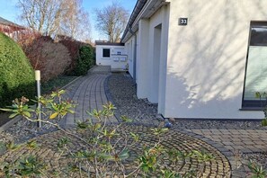 A pathway leading to a building with a number '33' sign, surrounded by greenery and a paved area. - Holiday apartment with 3 bedrooms (Schönberg (Holstein))
