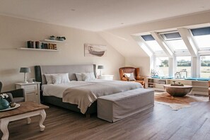 Une chambre à coucher avec un grand lit, des tables de chevet, une chaise, une table basse et une lucarne.