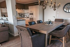Eine moderne Küche mit weißen Schränken, eine Essecke mit einem Holztisch und Ledersesseln sowie ein Kronleuchter.
