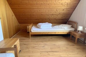 A bedroom with a wooden sloped ceiling, a single bed with white bedding, a small wooden nightstand with a lamp, and a wooden bench. - Holiday home in Langholz with swimming pool (Langholz)
